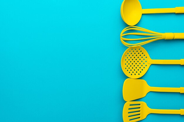 Yellow ladle whisk skimmer spatulas over turquoise blue table with copy space