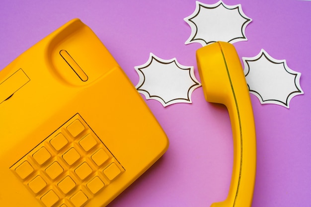 Yellow landline phone with speech bubble on purple surface