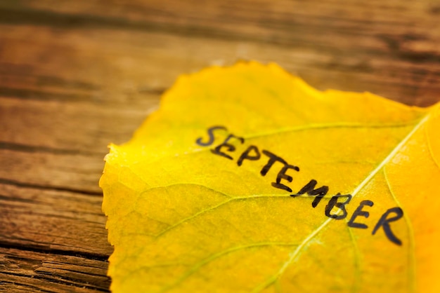 Yellow leaf with the inscription SEPTEMBER on the old wooden background with cracks