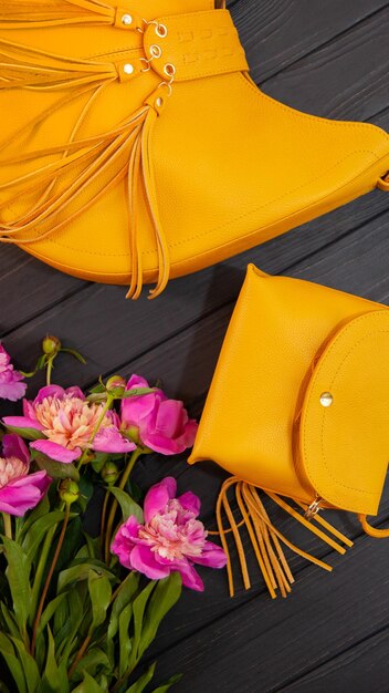 Yellow leather bag with peonies on a wooden background