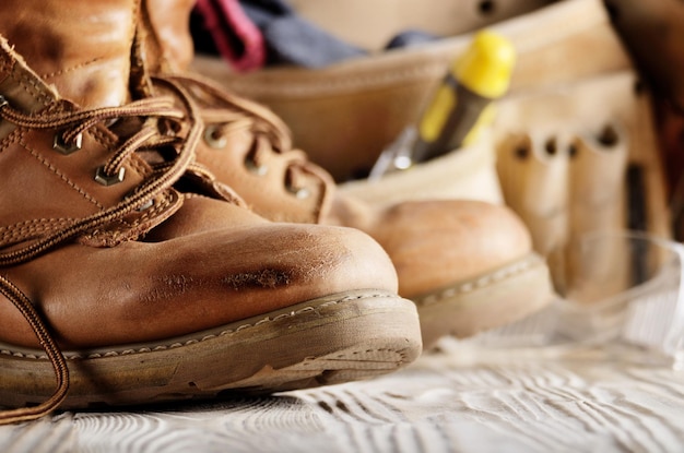 Yellow leather used work boots and tool belt on wooden background closeup. Place for text