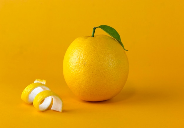 A yellow lemon fruit with leaf and peel slice isolated on yellow background