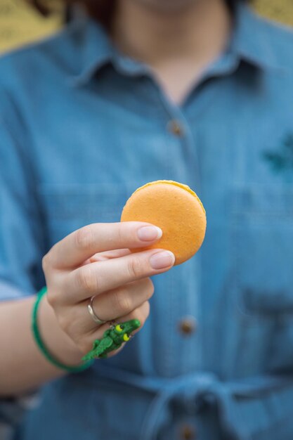 Фото Желтый лимонный печенье наполовину укушенное в руке близко к голубому фону кондитерская рука с макароном