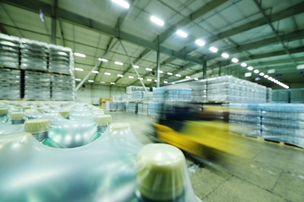 Yellow loader on the background of a huge industrial food warehouse with plastic PET bottles with beer, water, drinks. deliberate blurring