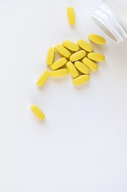 Yellow long vitamins lying next to pill jar on white background, macro, closeup, copy space