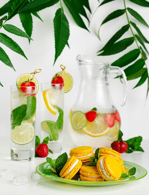 Foto amaretti gialli e limonata con lime, menta e fragole su uno spazio bianco. verticale