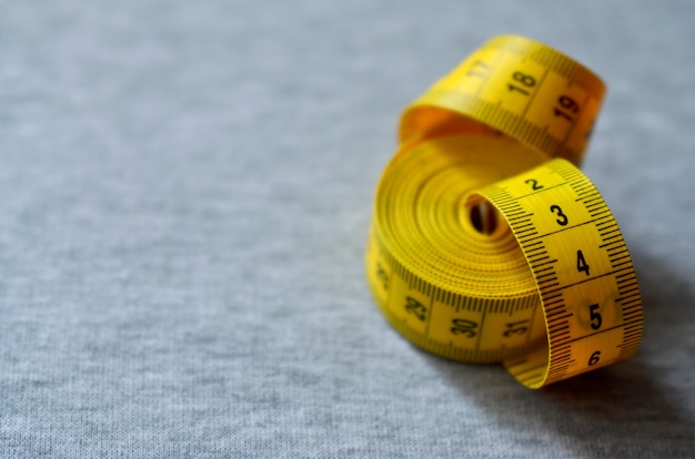 Yellow measuring tape lies on a gray knitted fabric