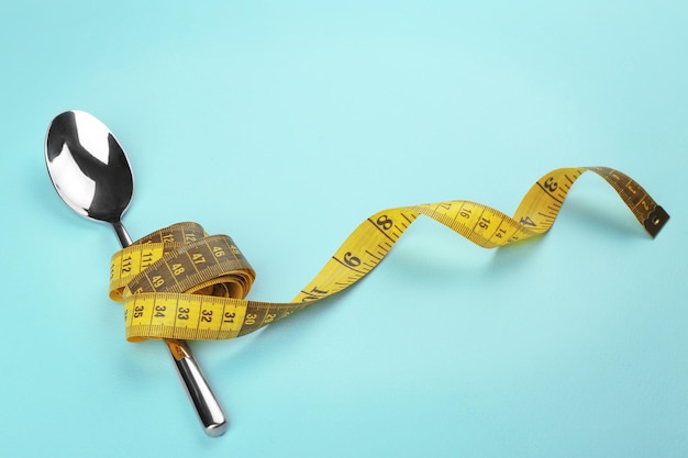 Yellow measuring tape wrapped around spoon lying on color surface Diet concept