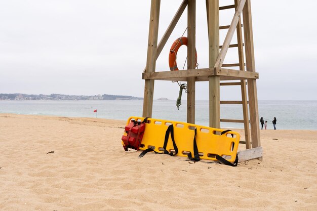 Photo yellow medical backboard leaning on wooden lifeguard tower on cloudy day in algarrobo beach chile