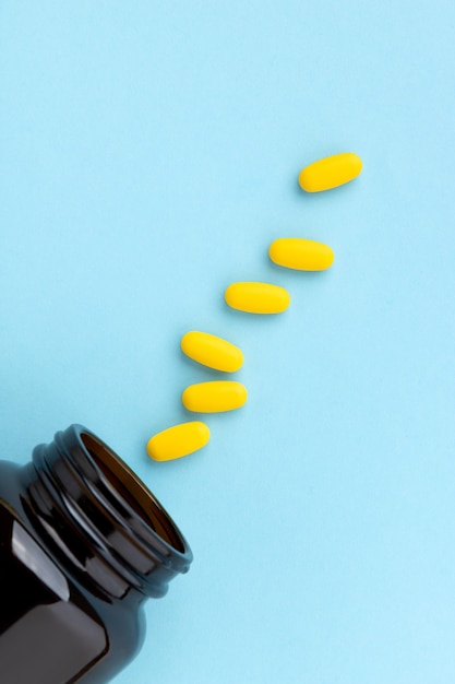 Yellow medical pills spilling out of a drug bottle on blue