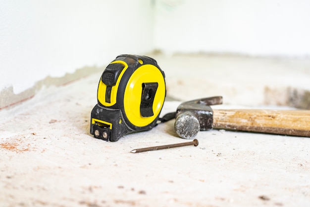 Yellow meter and steel hammer have nails placed on the cement floor.