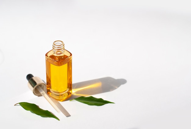 Yellow mock-up cosmetic oil on white background with green leaves and copy space