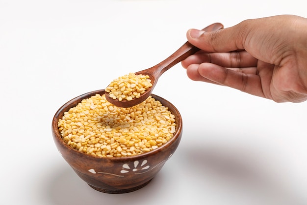 Yellow moong mung dal lentil pulse bean in wooden and spoon bowl on white background