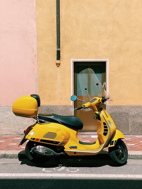 Foto scooter a motore giallo parcheggiato in una strada di fronte a un muro giallo con luce solare e spazio di copia