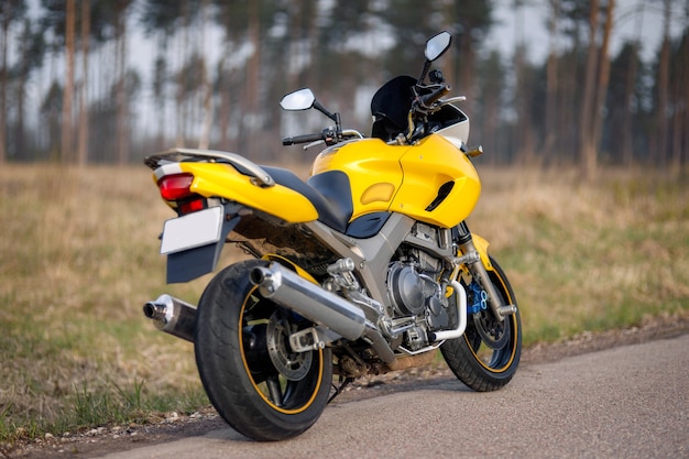 Yellow motorcycle on the road in the forest zone, rear-side view