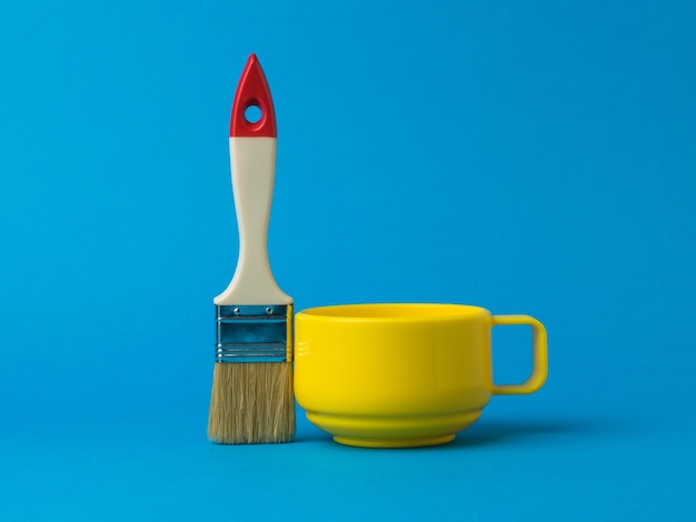 Yellow mug and brush with long bristles on a blue background. The color trend.