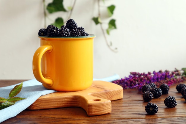 Yellow mug of fresh blackberries closeup on a wooden board among scattered blackberries bokeh space for text