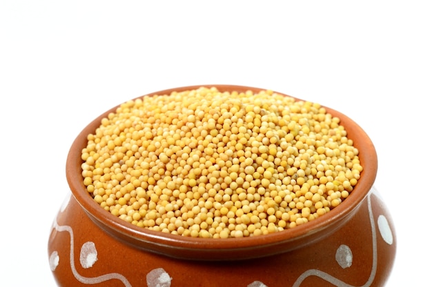 Yellow mustard seeds in clay pot isolated on white background