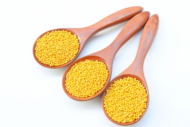 yellow mustard seeds in the wooden spoon on White background