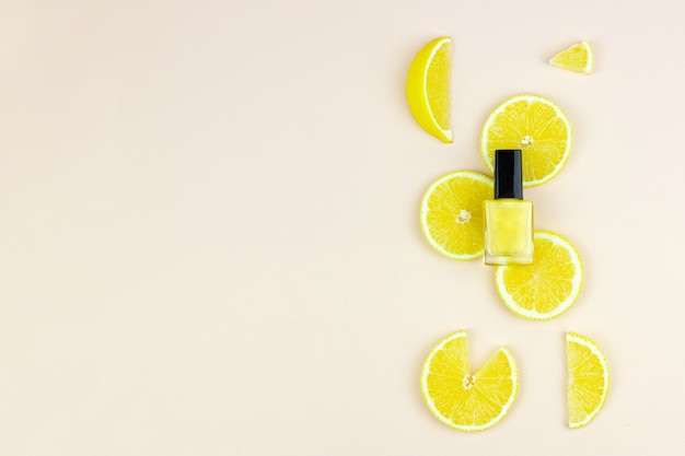 Yellow nail polish bottle on lemon pieces, light background. Manicure tools, beauty, nail art concept.