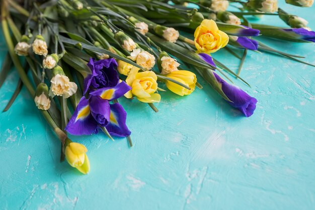 青い背景に分離されたラインフラワーアレンジメントの黄色い水仙の花と紫色の菖蒲。美しい春の花幸せな母の日。コピースペース