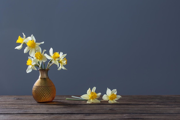 Yellow narcissus  in vase on wooden table on dark background