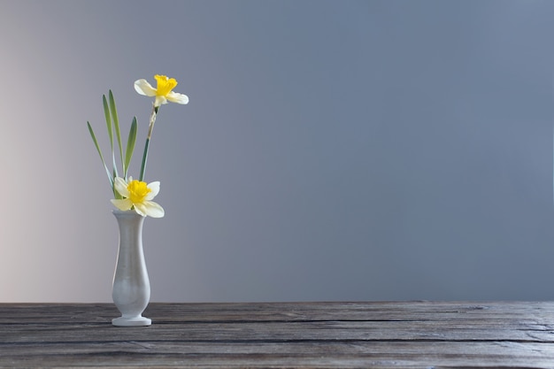 Yellow narcissus  in vase on wooden table on dark background