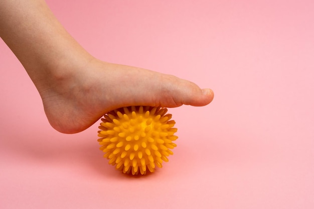 Yellow needle ball for massage and physical therapy on a pink background with a child39s foot the concept of prevention and treatment of foot valgus