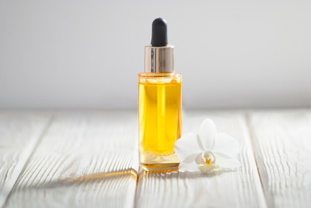 Yellow oil in the glass bottle with orchid flower and white towel