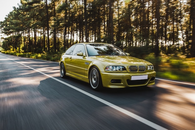 Yellow old model sedan driving in the forest road. front view