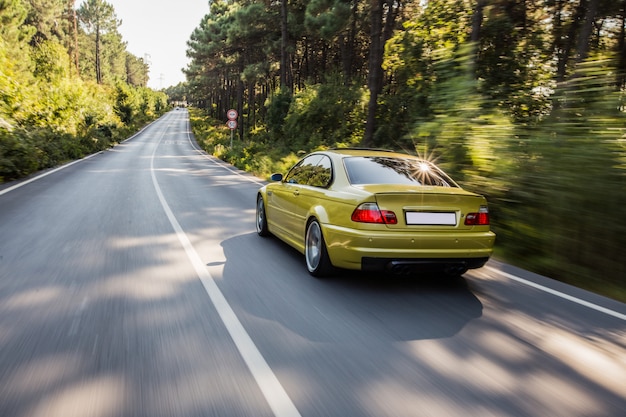 Yellow old model sedan driving in the forest road