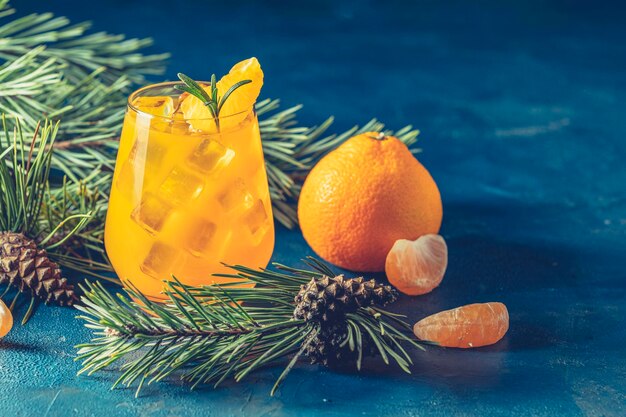 Yellow orange cocktail with tangerine and rosemary in glass on dark blue concrete background decorated pine branches with cones close up Christmas and New Year holiday welcome drink