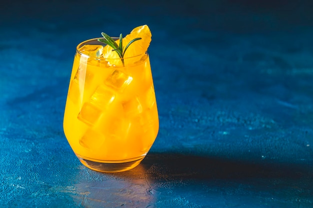 Yellow orange cocktail with tangerine and rosemary with ice in glass on dark blue concrete background close up Christmas and New Year holiday welcome drink