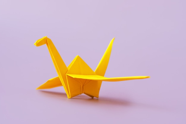 Yellow origami bird on purple surface