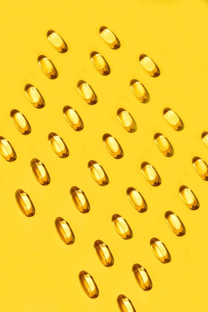 黄色の楕円形の錠剤は、黄色のビタミンオメガ3シームレスパターンをカプセル化します