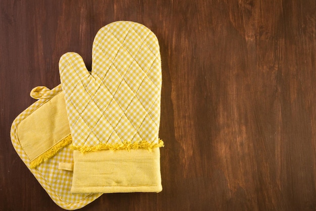 Photo yellow oven mitt on wood background.