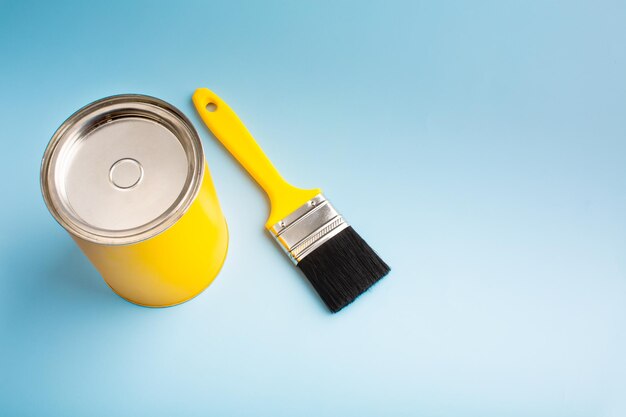 Photo yellow paint in a jar with a brush on a blue background