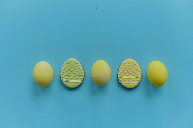 Yellow painted chicken eggs and cookies eggs on a blue backgroung Top view