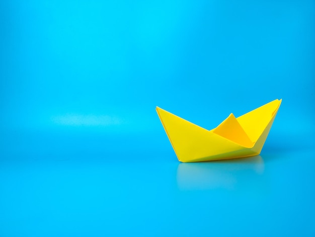 リーダーシップのチームワークと勝利の成功のための青い背景のコンセプトに黄色い紙の船