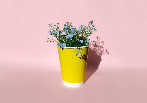 Yellow paper cup with field blue flowers on pink background