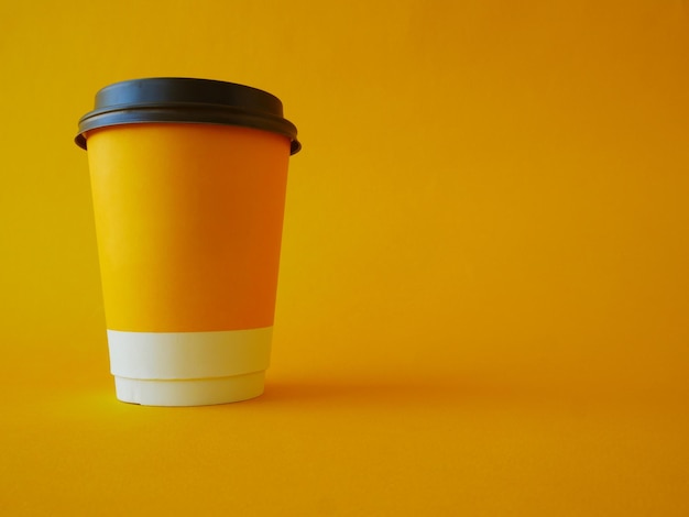 A yellow paper disposable cup with a black plastic lid on a yellow background with