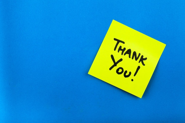 Yellow paper sticker note  with text thank you on blue background