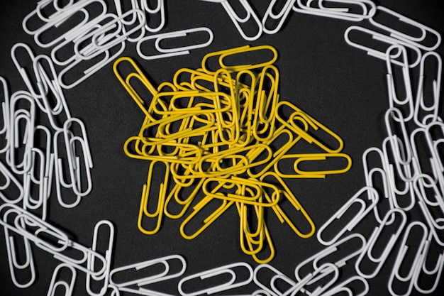 Yellow paperclip isolated in the frame made of white paperclip paperclip on black background