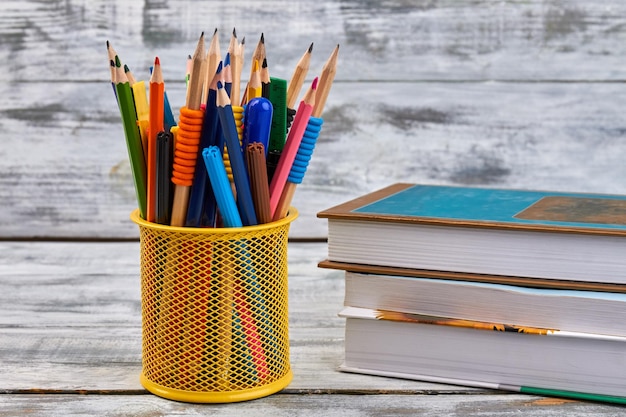 Yellow pen holder with stack of books on white desk back to school concept