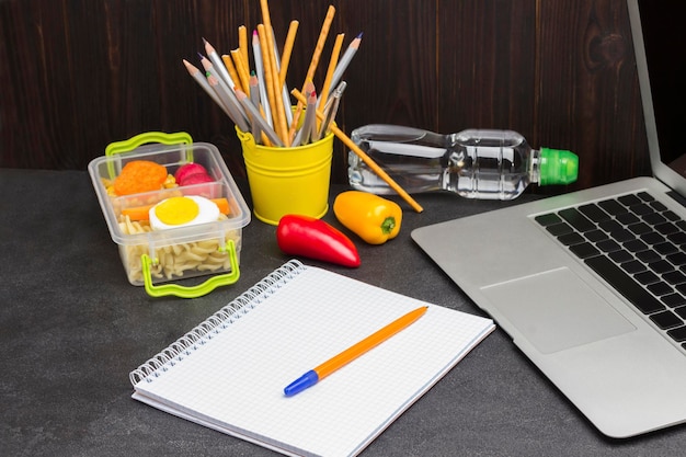 Yellow pen on notebook with springs Bottle of water Launch Box Bucket of pencils and Laptop