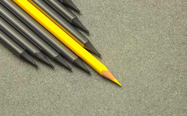 A yellow pencil that stands out from the crowd of many identical blacks Leadership uniqueness