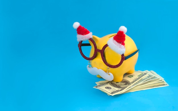 Yellow piggy bank in Santa Claus glasses with money. Creative composition with a piggy bank. The concept of Christmas bank shares and deposits. Festive New Year and Christmas shopping.