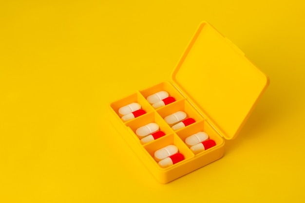 Yellow pillbox with pills on a yellow background