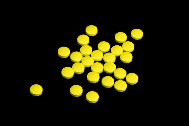 Yellow pills are scattered on a black background