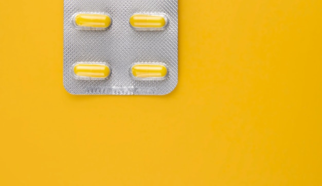 Yellow pills in a blister pack on a yellow wall copy space.